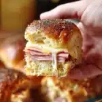 Hand holding a Ham and Havarti Cheese Slider with melty Havarti cheese stretching from the baked rolls.