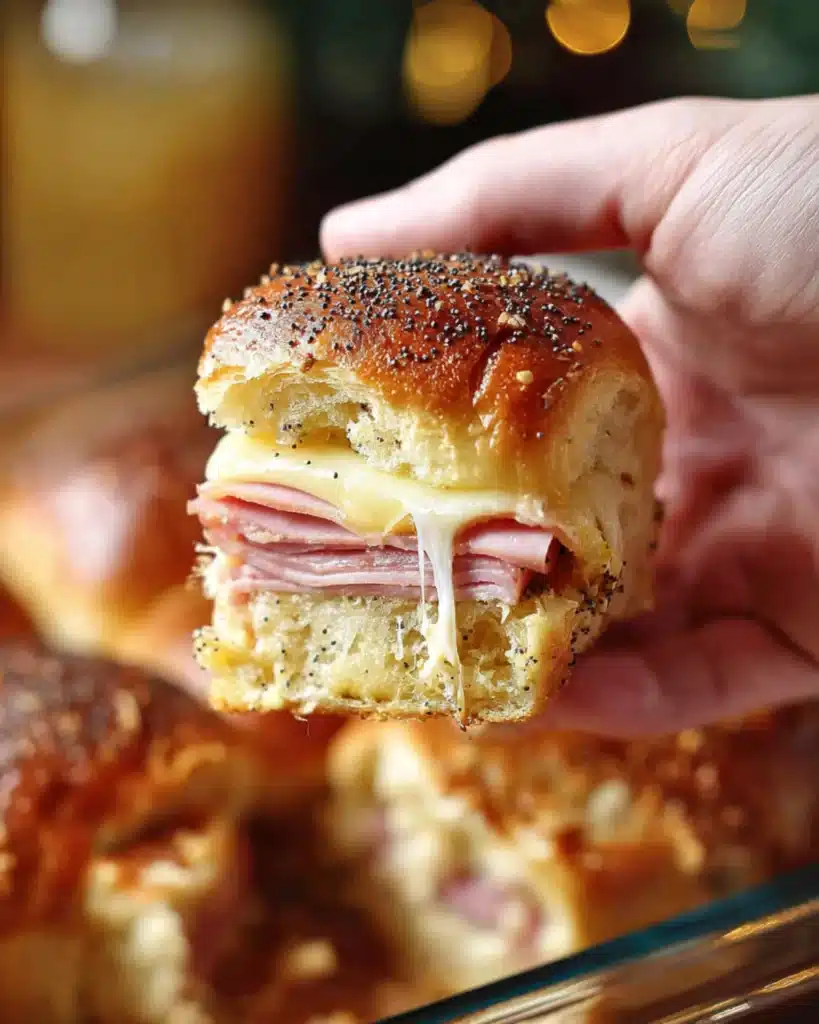 Hand holding a Ham and Havarti Cheese Slider with melty Havarti cheese stretching from the baked rolls.