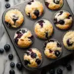 Golden blueberry protein muffins baked in a dark muffin tin on marble background.