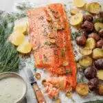 Cooked salmon fillet with roasted potatoes, fresh dill, lemon wedges, and creamy sauce.