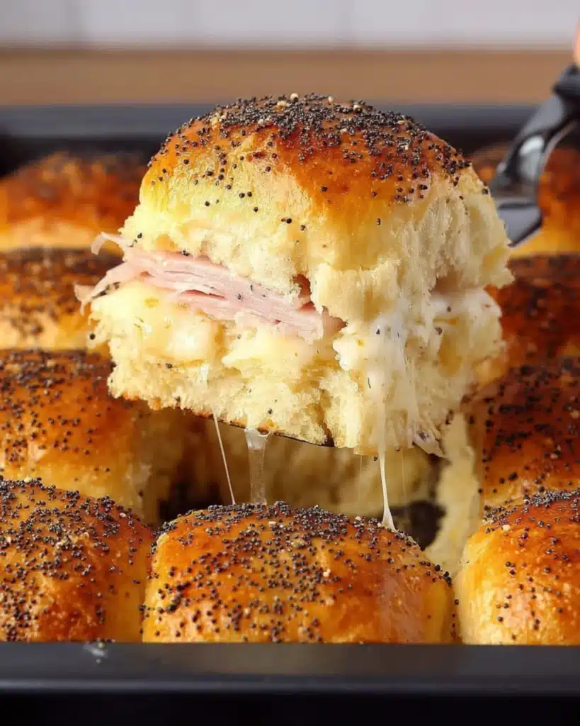 A hot Ham and Havarti Cheese Slider being lifted from a baking dish with melted cheese stretching underneath.