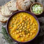 Pumpkin and Leek Soup served in a rustic purple bowl with crusty bread and sliced leeks on a wooden table