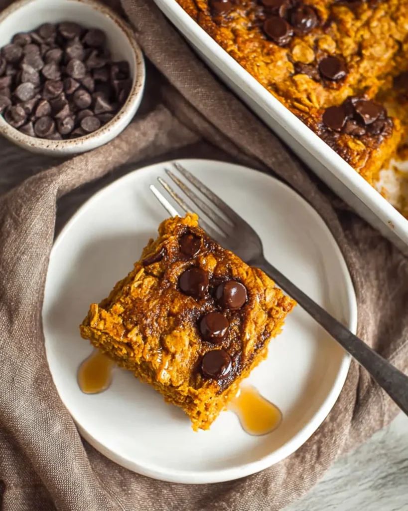 Pumpkin baked oatmeal slice topped with chocolate chips and maple syrup on a white plate