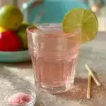 Pink salt detox drink in a glass with a lime slice and a small bowl of pink salt.