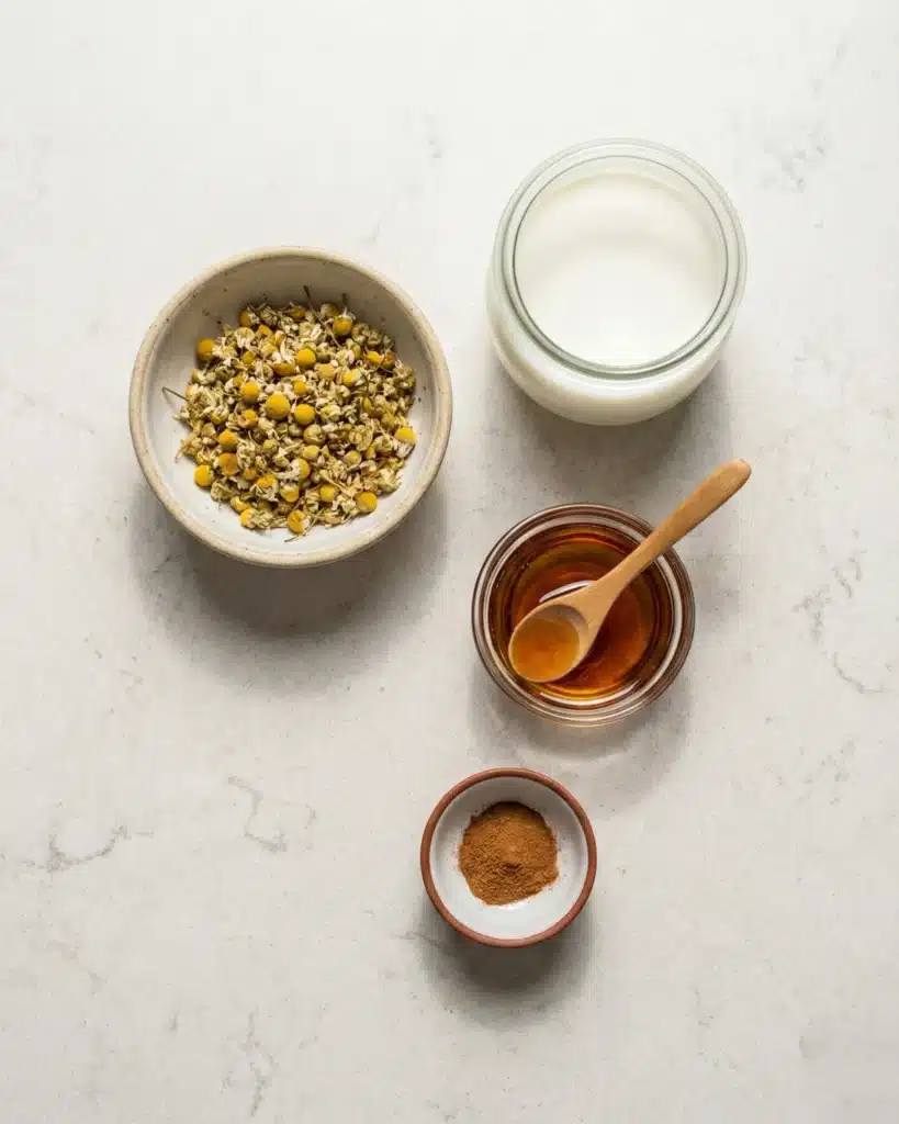 Flat lay of chamomile, milk, honey, and cinnamon arranged on a marble surface.