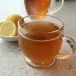Glass cup of collagen gelatin tea with lemon slices in the background on a bright countertop.