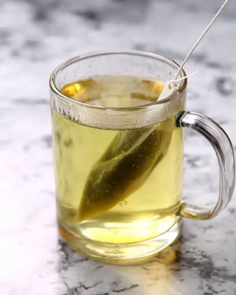 Brewing green tea bag in a transparent mug on marble surface