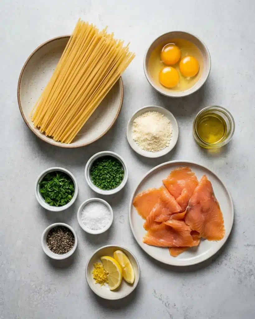 Flat lay of smoked salmon carbonara ingredients including pasta, eggs, Parmesan, herbs, and lemon.