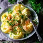 Plate of smoked salmon carbonara pasta with parsley garnish and lemon wedges on rustic wood surface.