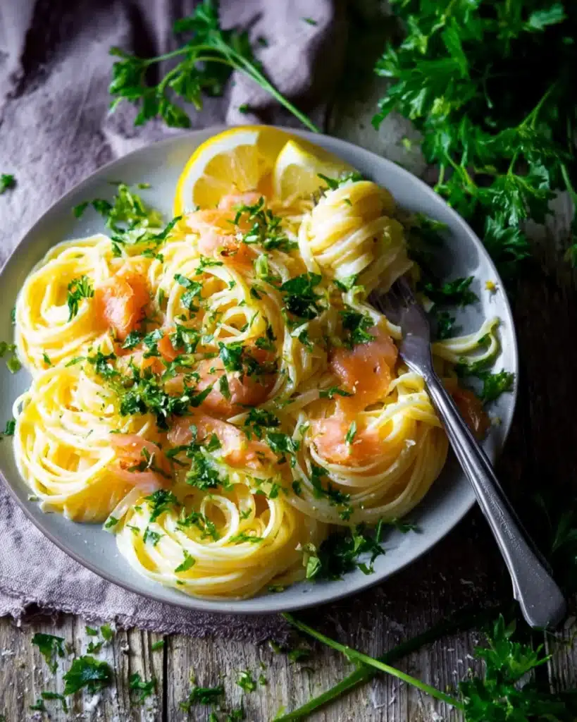 Plate of smoked salmon carbonara pasta with parsley garnish and lemon wedges on rustic wood surface.