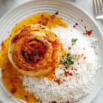 Roasted whole onion served with fluffy white rice and spicy Cajun butter sauce on a white plate