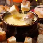 Classic cheese fondue in a ceramic pot with melted cheese and bread on fondue forks