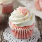 Pink velvet cupcake with white cream cheese frosting and pink sugar pearls on a lace doily
