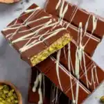 Overhead shot of pistachio chocolate bars topped with white chocolate drizzle on marble surface.