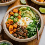 High protein dinner bowl made with ground beef, avocado, and roasted sweet potatoes served with creamy sauce and herbs