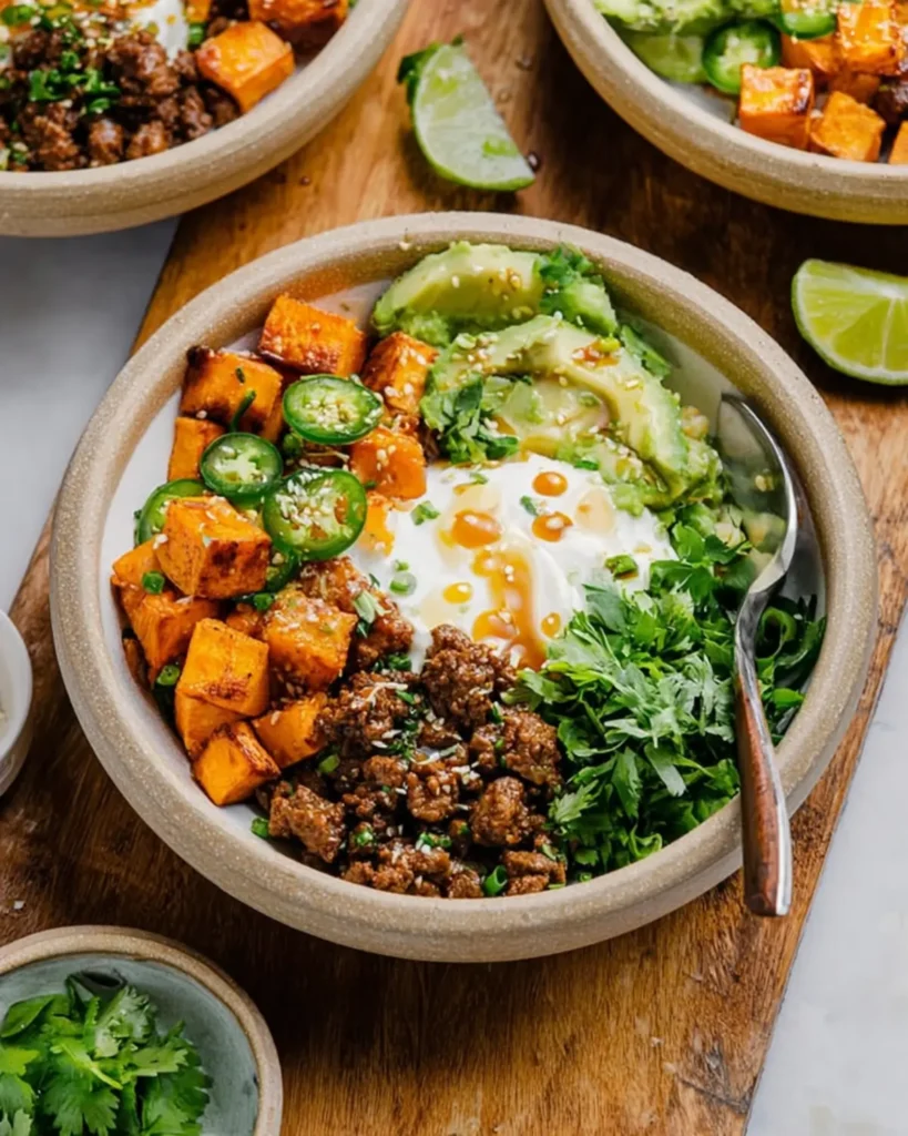 High protein dinner bowl made with ground beef, avocado, and roasted sweet potatoes served with creamy sauce and herbs