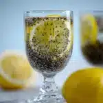 A glass of lemon chia seed drink on a white background with fresh lemons in the frame.