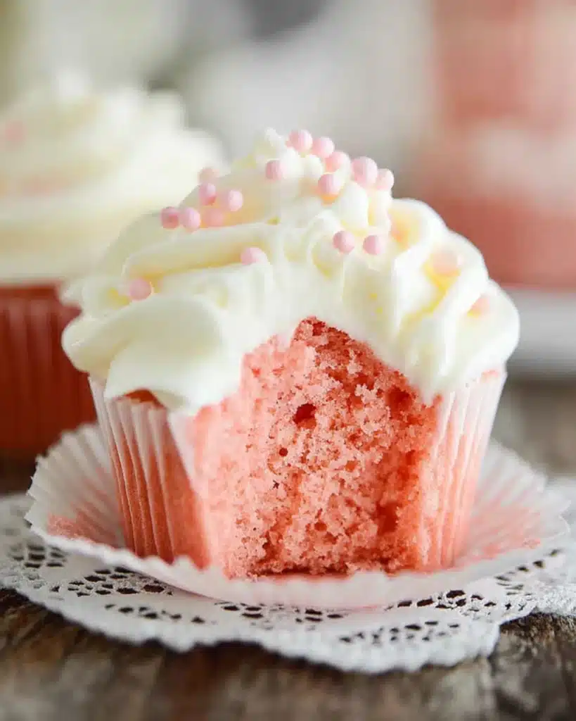 Close-up of a bitten pink velvet cupcake with creamy frosting and pink sprinkles on a lace doily