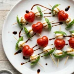 Heart shaped tomato mozzarella basil skewers drizzled with balsamic glaze on a white plate.