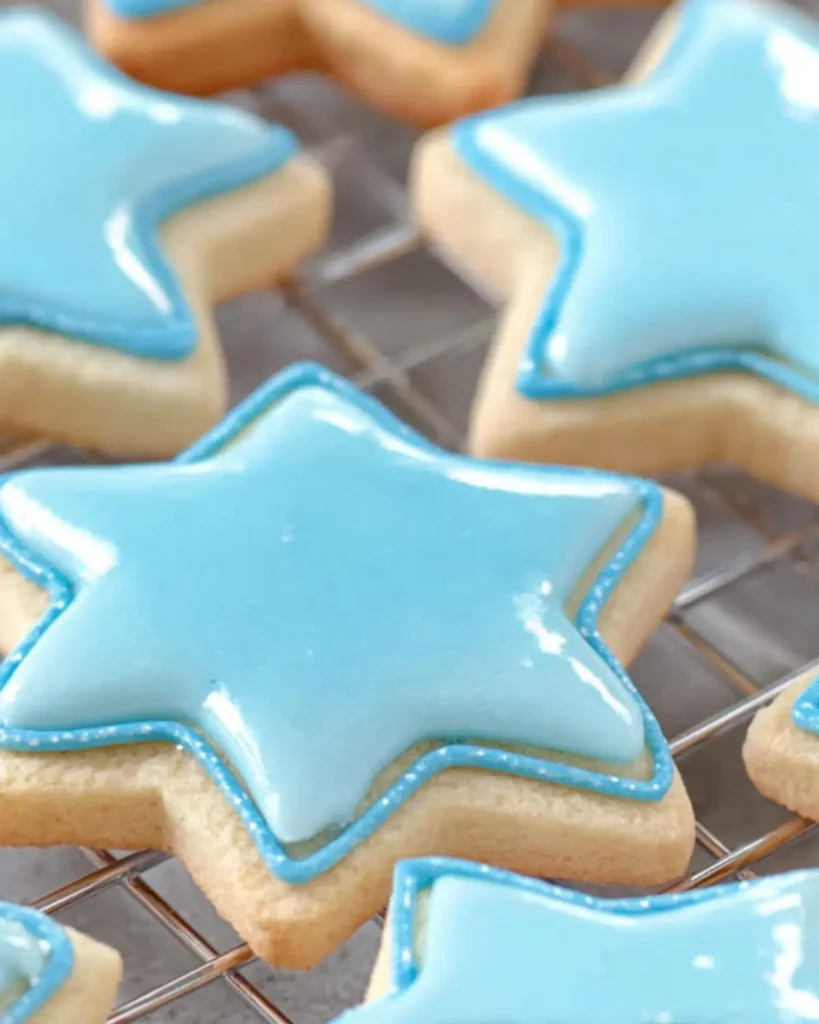 Star shaped cookies topped with smooth blue sugar cookie icing on a wire cooling rack