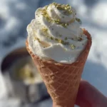 Close-up of waffle cone filled with whipped snow ice cream and pistachio pieces held in natural daylight