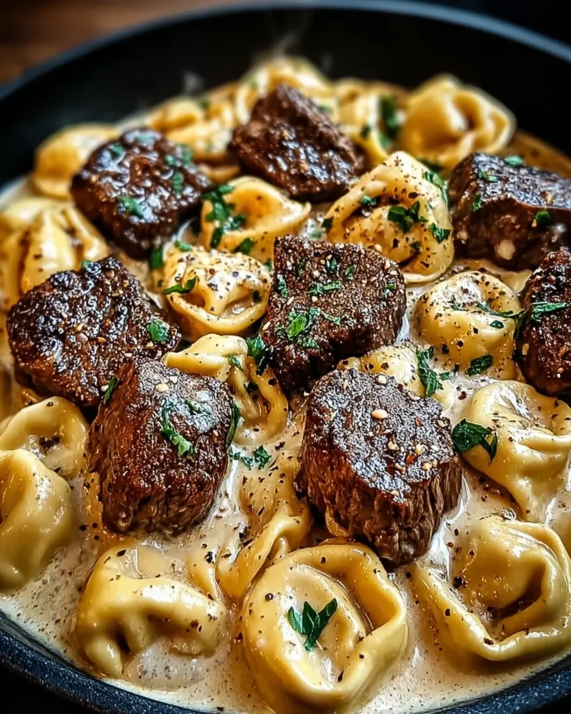 Close up of seared steak medallions with cheese tortellini in thick cream sauce topped with fresh parsley