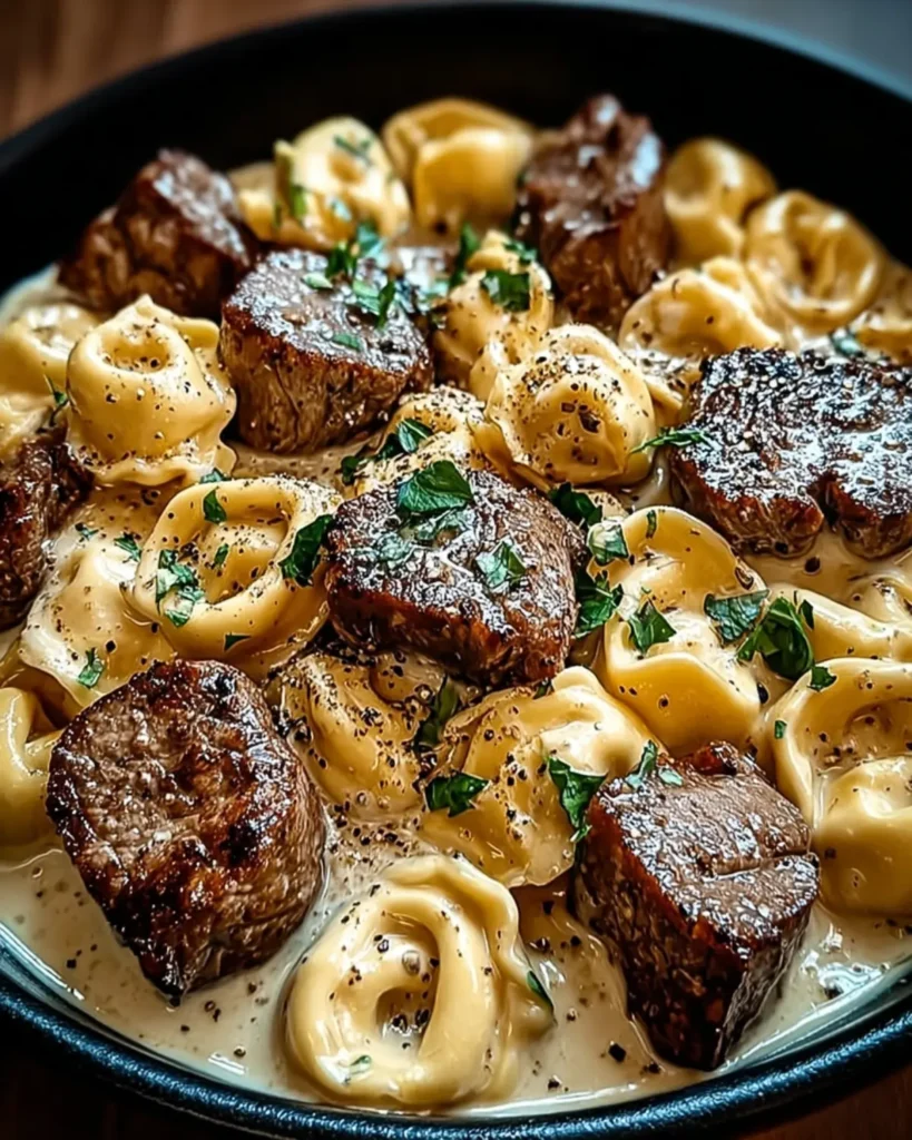 Creamy tortellini and steak bites cooking together in a covered skillet on wooden table