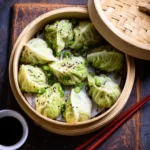 Hand holding cabbage dumpling with chopsticks above bamboo steamer