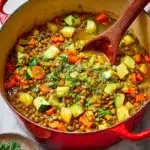 A rustic vegetable stew in a red pot with chopped parsley scattered on top