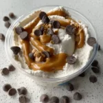 Creamy ice cream topped with peanut butter drizzle and chocolate chips on a speckled countertop.