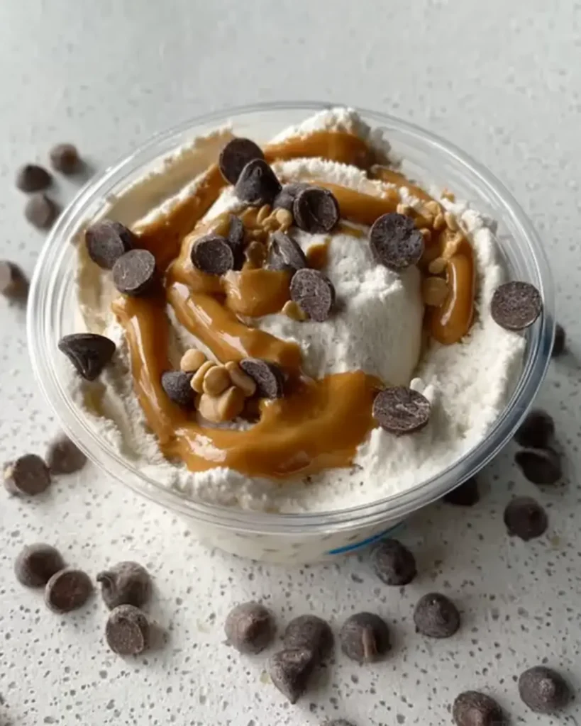 Creamy ice cream topped with peanut butter drizzle and chocolate chips on a speckled countertop.