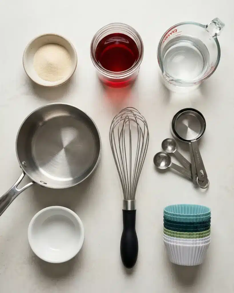 Ingredients and tools arranged neatly for making homemade pink gelatin including juice gelatin powder whisk and molds