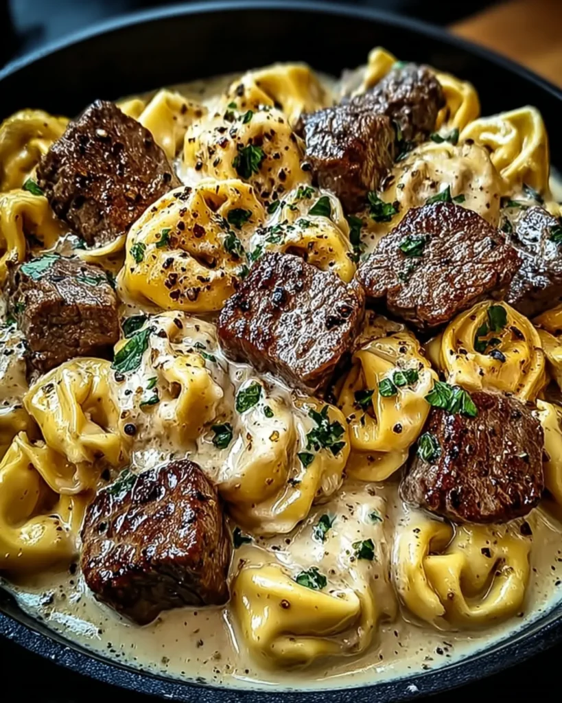 Close view of creamy tortellini with seared beef chunks and cracked pepper in rich sauce