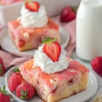 Strawberry earthquake cake slice topped with whipped cream and fresh strawberry on white plate