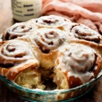 Freshly baked cinnamon roll recipe in a glass pie dish topped with thick cream cheese icing