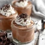 Small glass jars filled with creamy chocolate mousse topped with whipped cream and chocolate curls