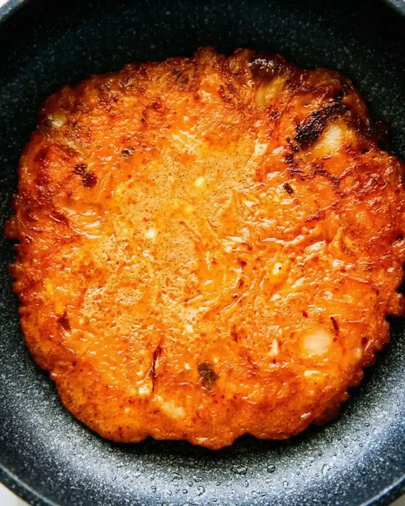 Savory kimchi pancake cooking in a nonstick pan with golden caramelized surface
