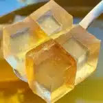 Golden translucent tea jelly cubes resting on a spoon above warm brewed tea