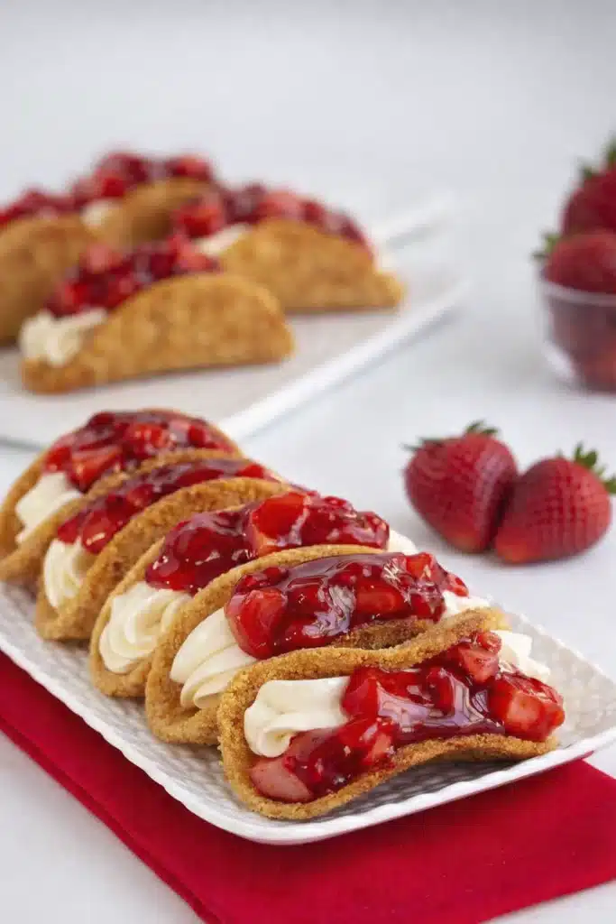 close up of cheesecake tacos with creamy filling and strawberry topping in crispy graham cracker shells