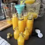 Turmeric ginger lemon shots being poured into small glass bottles using a funnel for storage