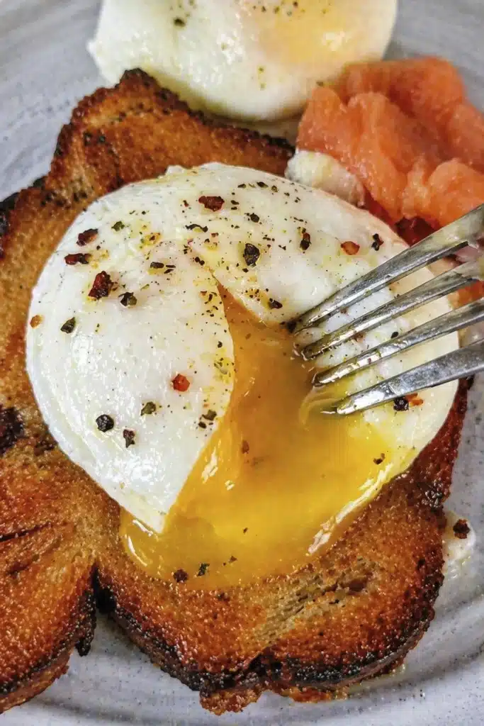Close up of air fryer poached egg with golden runny yolk flowing over crispy toast