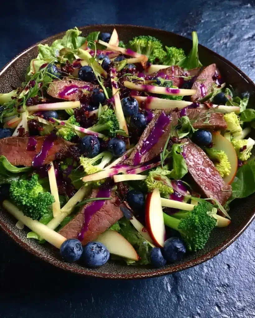 Fresh salad with beef slices, blueberries, apple sticks, and purple dressing