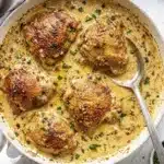 Golden seared chicken thighs in a creamy garlic sauce with herbs in a skillet