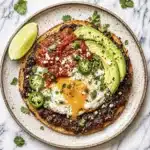 Huevos rancheros recipe with fried egg, avocado slices, black beans, and salsa on crispy corn tortilla