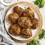 Oven Baked Chicken Thighs served on plate with herbs and crispy golden skin