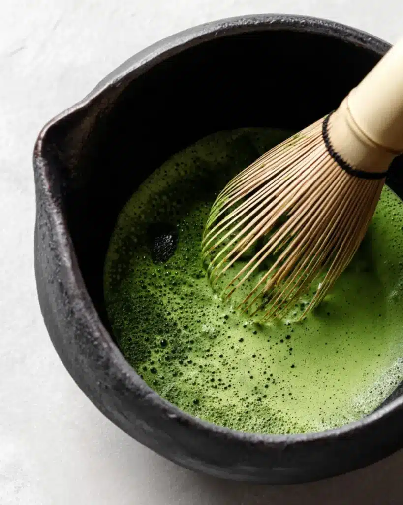 Bamboo whisk mixing green tea in a bowl with frothy texture