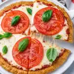 Close up of tomato basil pizza with a slice being lifted showing melted cheese stretch