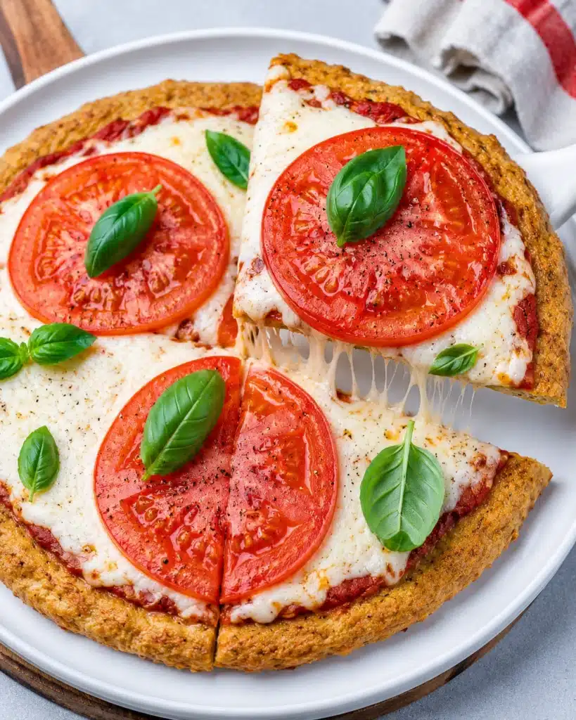 Close up of tomato basil pizza with a slice being lifted showing melted cheese stretch