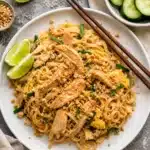 Rice noodles with chicken, scrambled eggs and peanuts served on a white plate with chopsticks