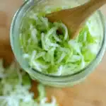close up of shredded cabbage inside a jar being pressed with a wooden spoon